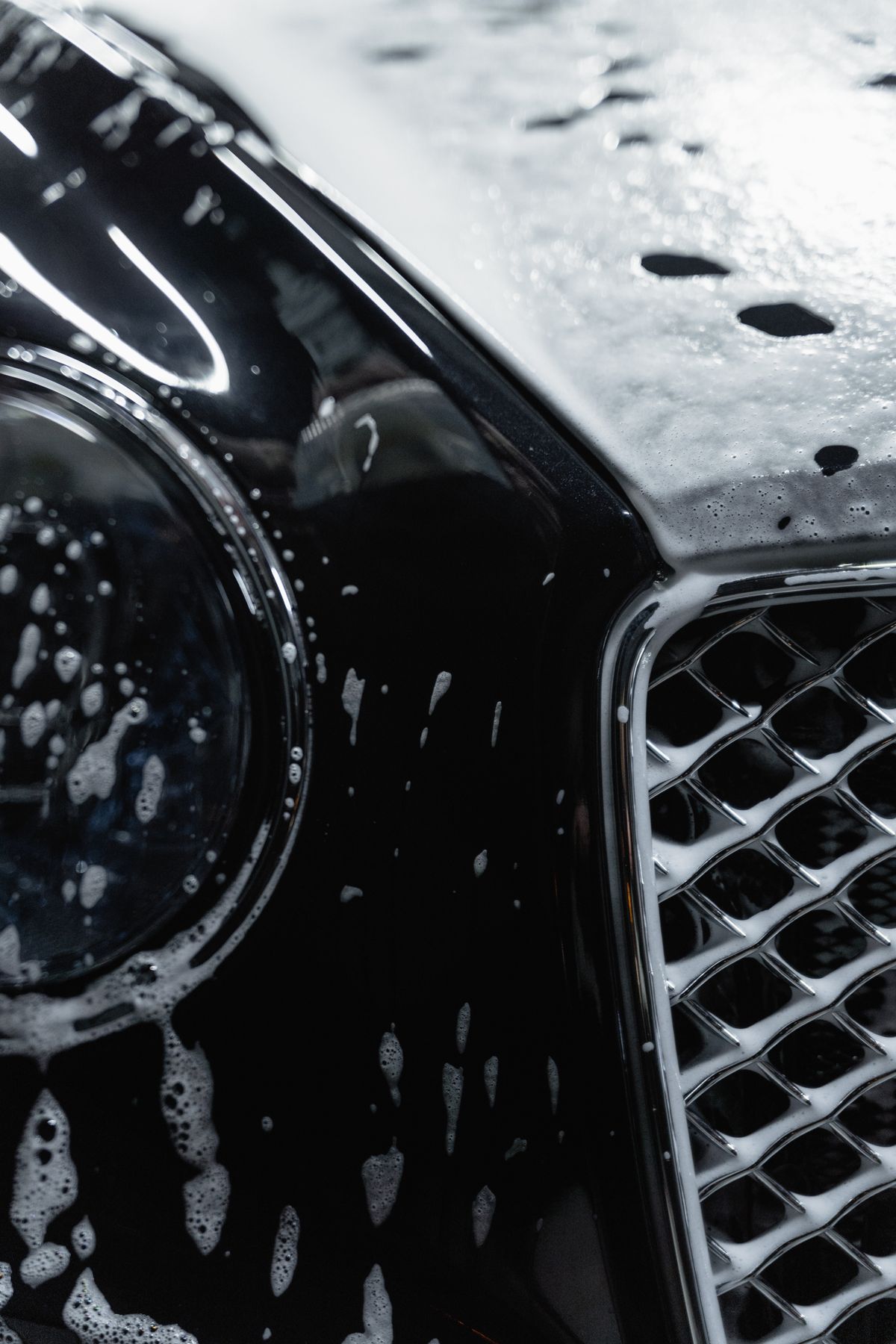 Detailer rinsing thick foam off a car during a wash